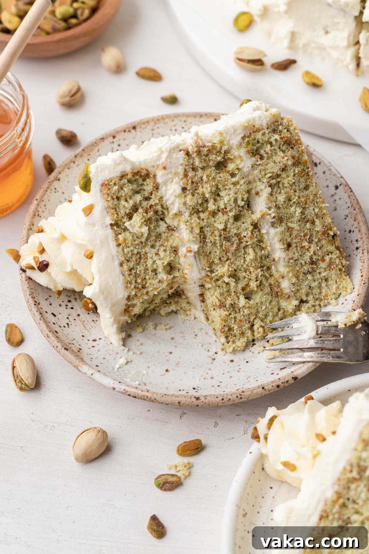 Velvet Pistachio Indulgence 6 A slice of pistachio layer cake on a speckled white dessert plate, with a bite missing.