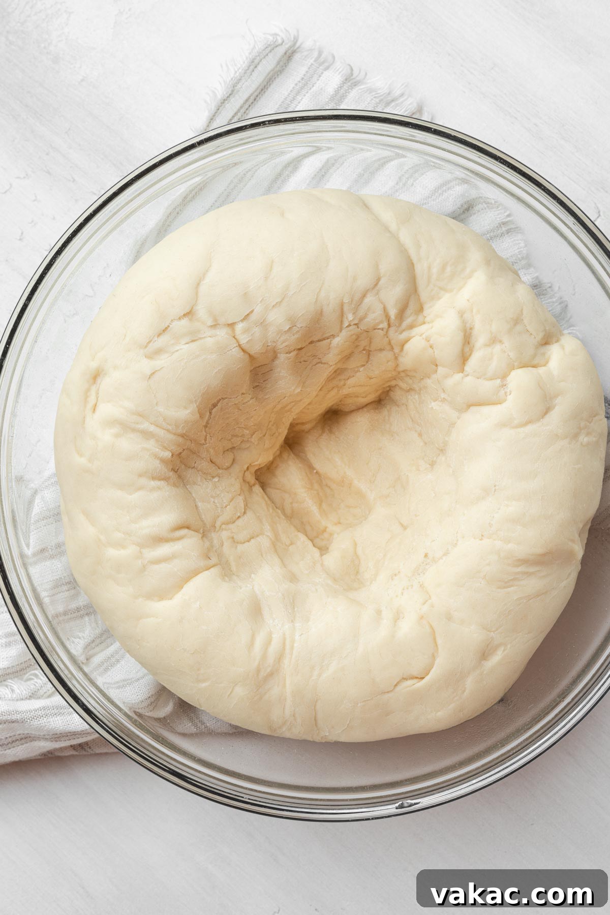 An overhead view of bread dough that has risen and been gently punched down in a glass mixing bowl.