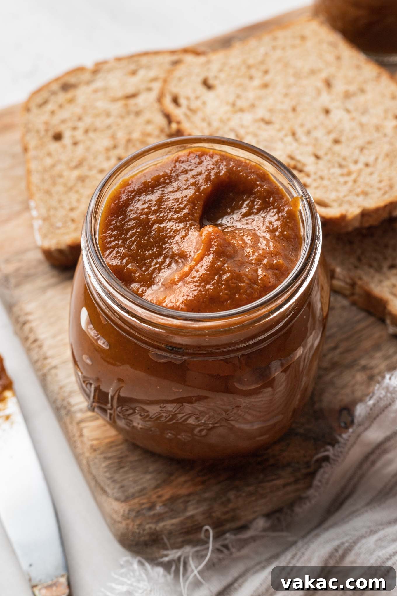 Golden Pumpkin Butter 2 A jar of pumpkin butter on a wooden cutting board with two pieces of bread.