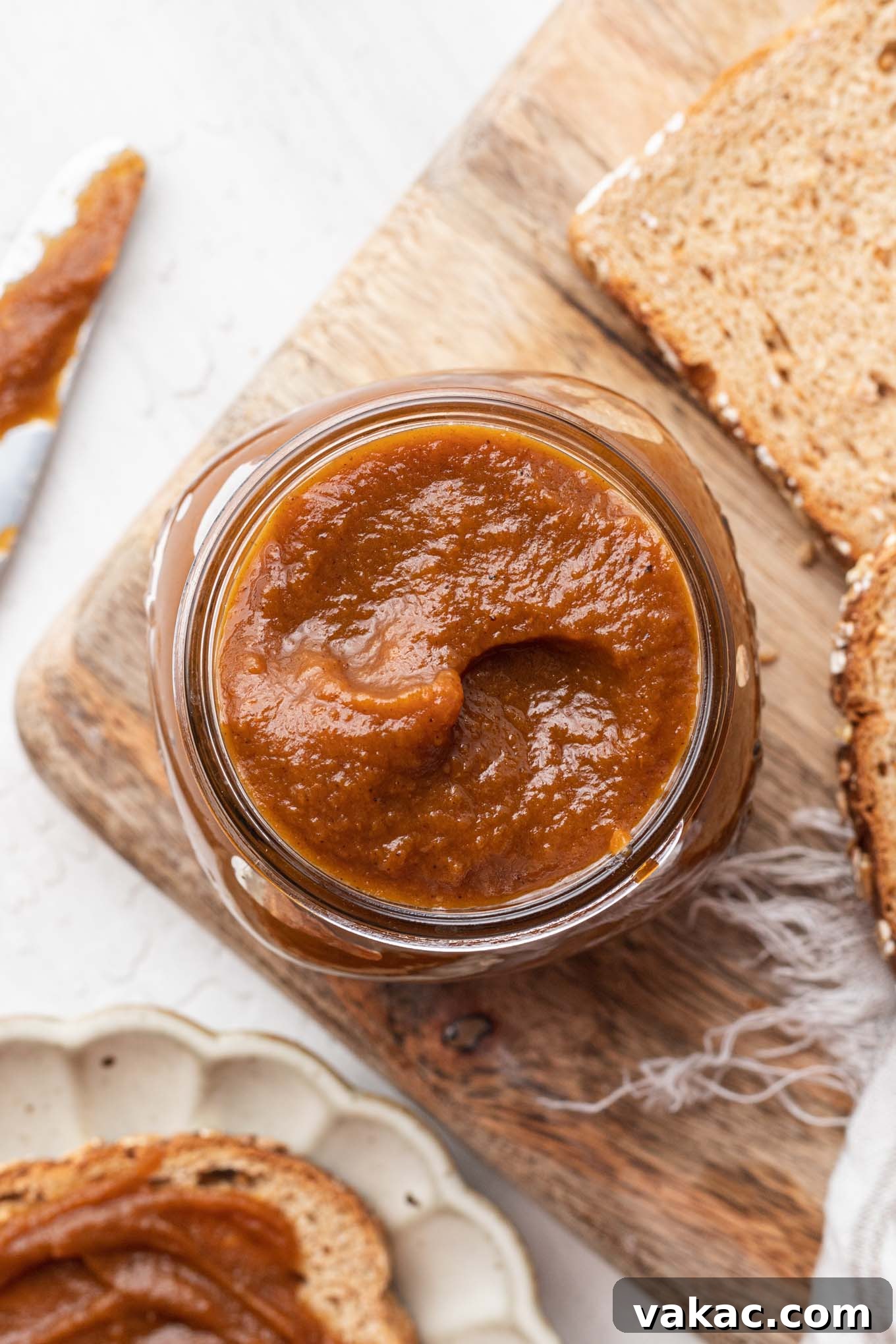 Golden Pumpkin Butter 4 An overhead view of a jar of pumpkin butter on a wood board with bread slices.
