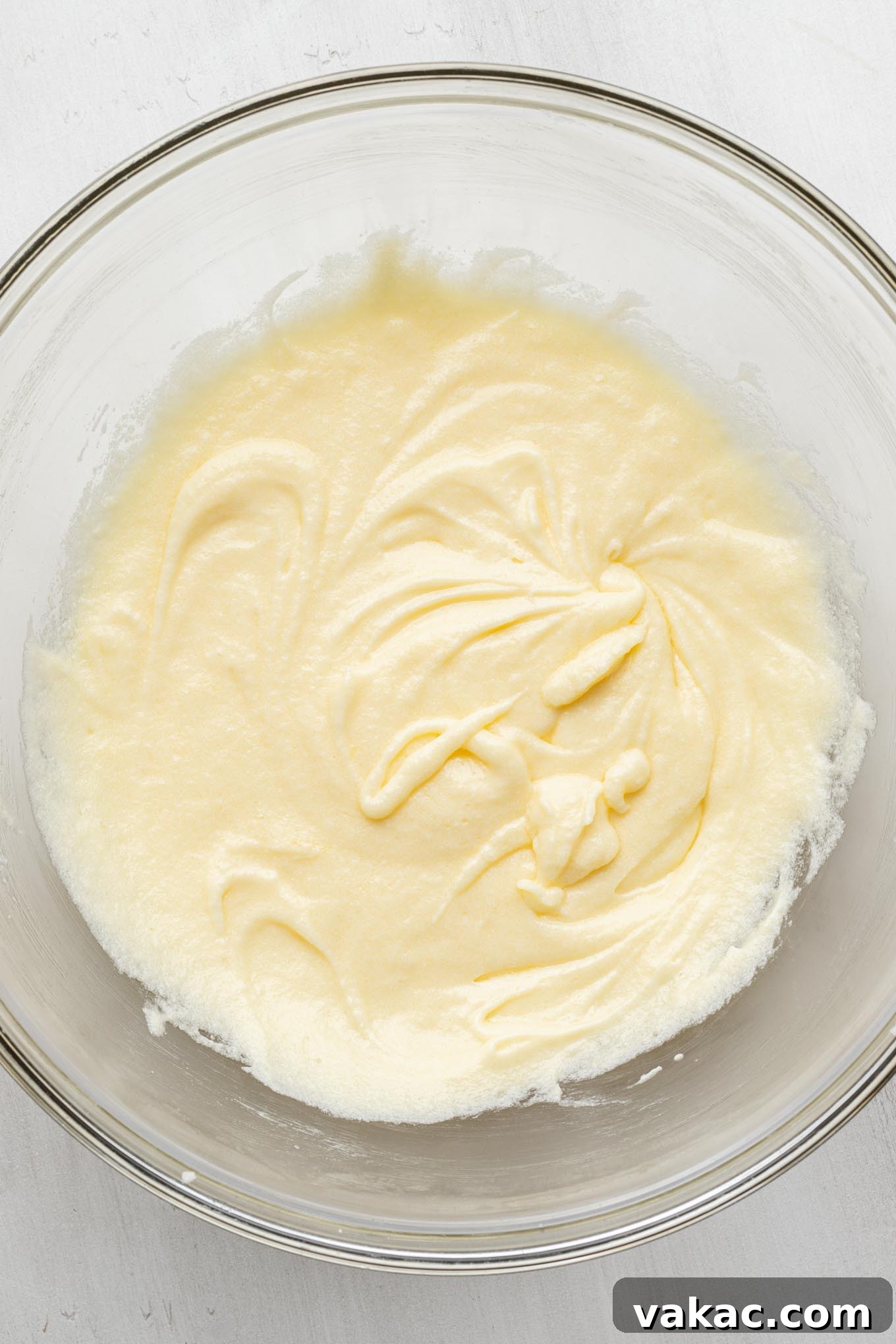 An overhead view of the wet ingredients for a vanilla cake in a glass mixing bowl, showcasing the rich liquid consistency.