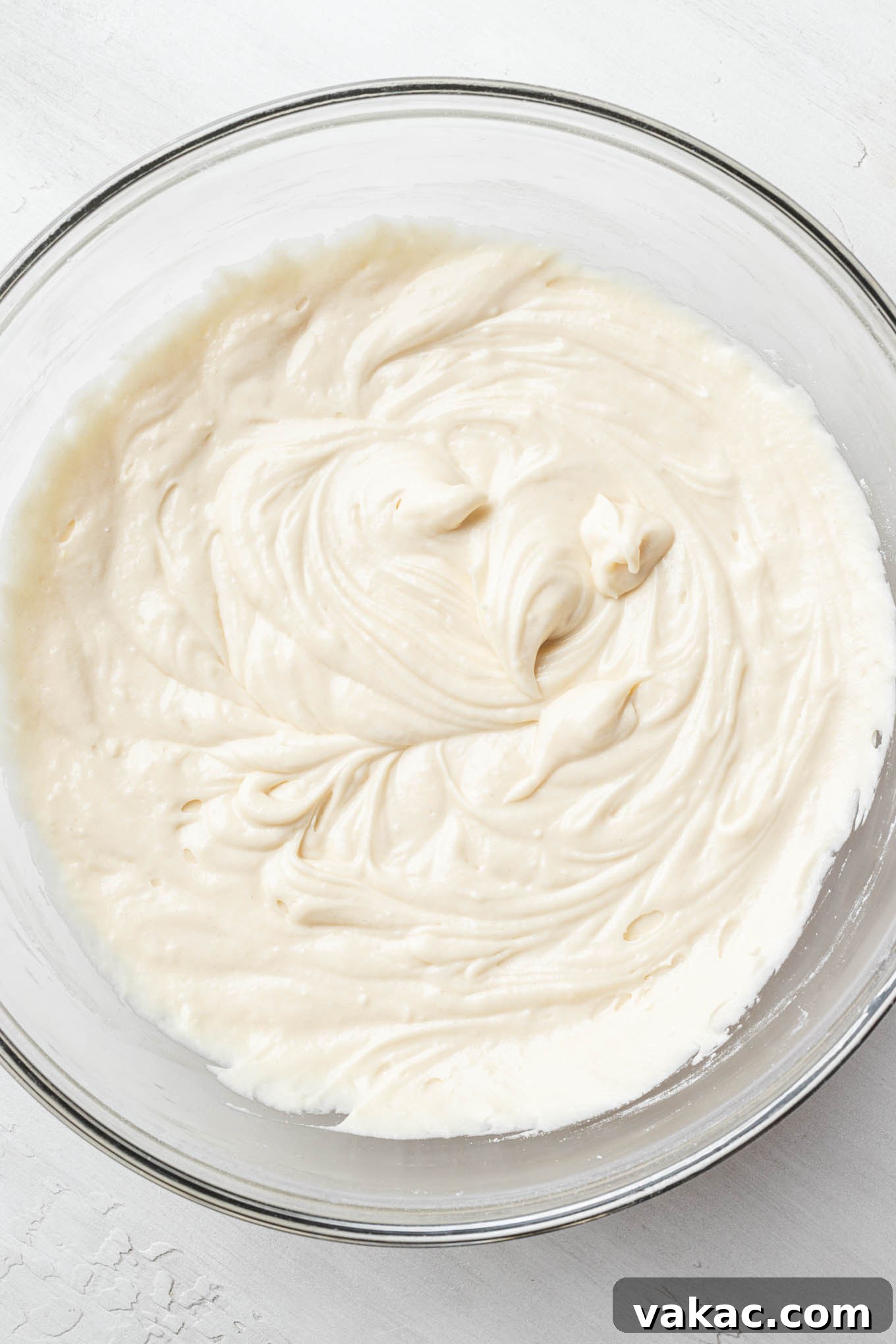 An overhead view of smooth, creamy vanilla cake batter in a glass mixing bowl, ready for baking.