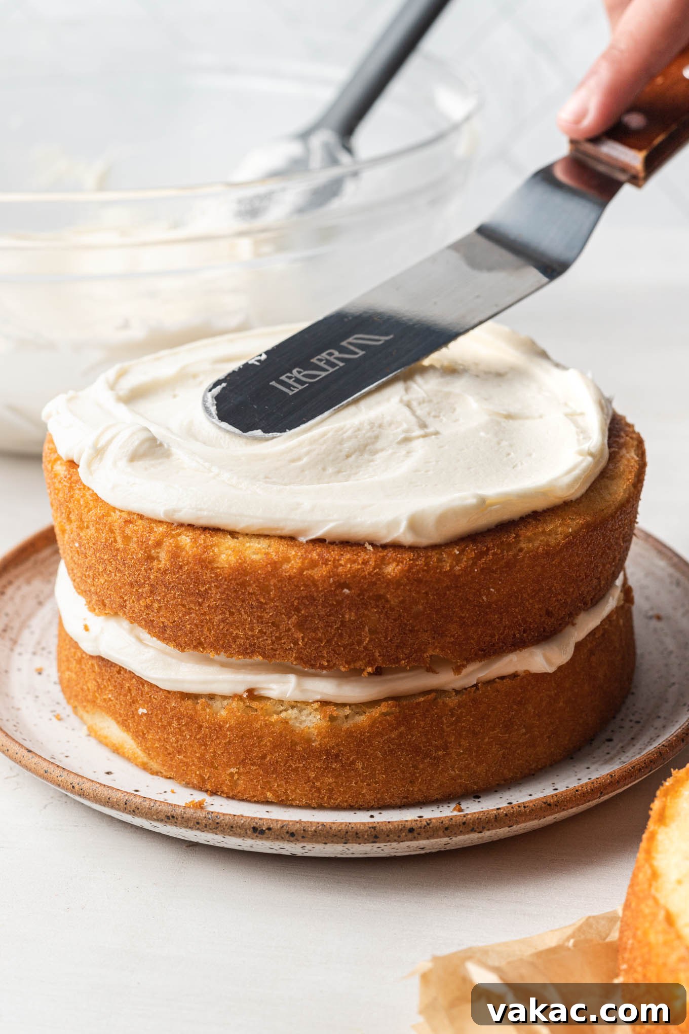 A 6-inch vanilla cake on a plate being meticulously assembled and frosted, showing the delicate layering process.