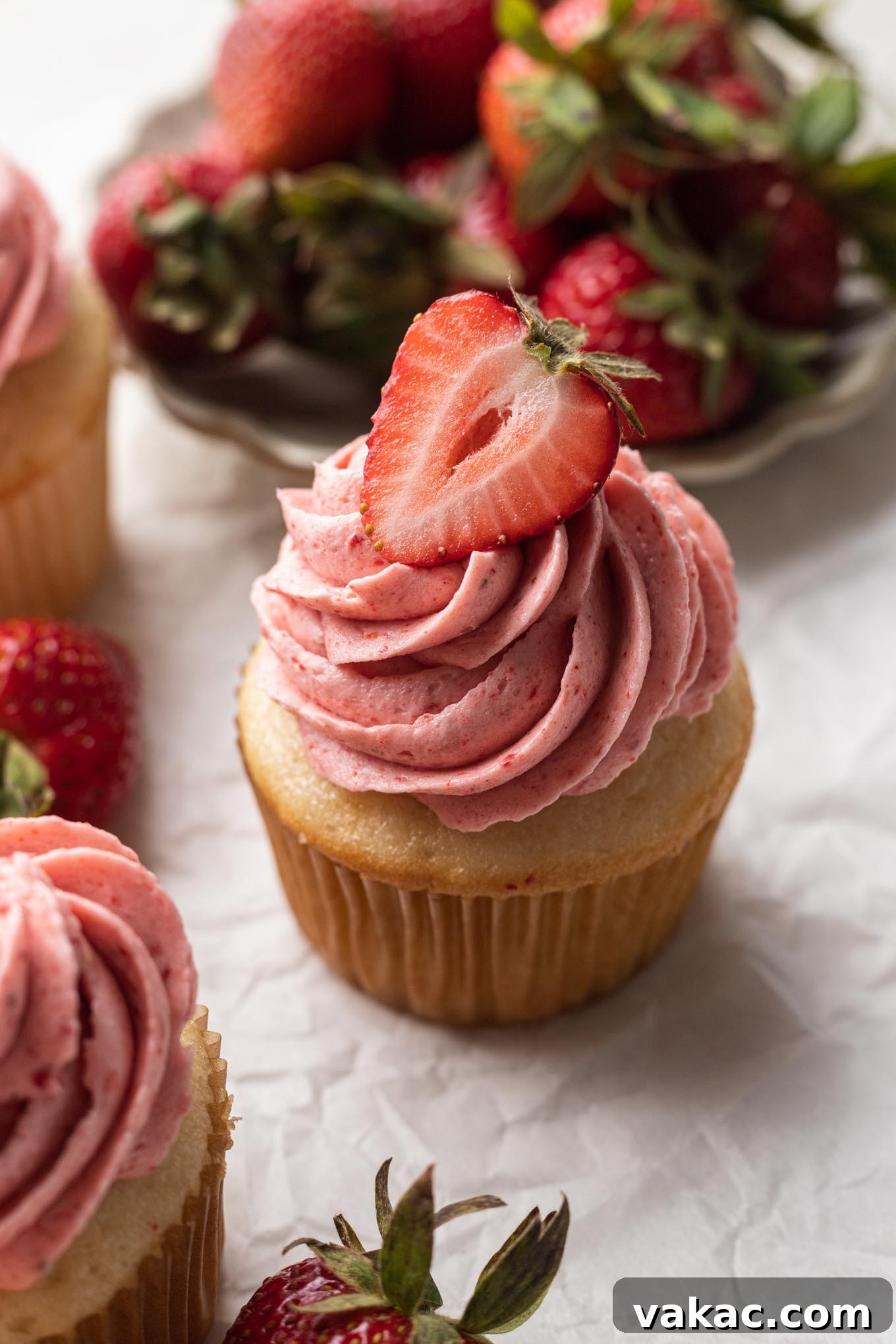 Velvet Strawberry Frosting 2 A vanilla cupcake topped with strawberry frosting and garnished with a fresh strawberry half.