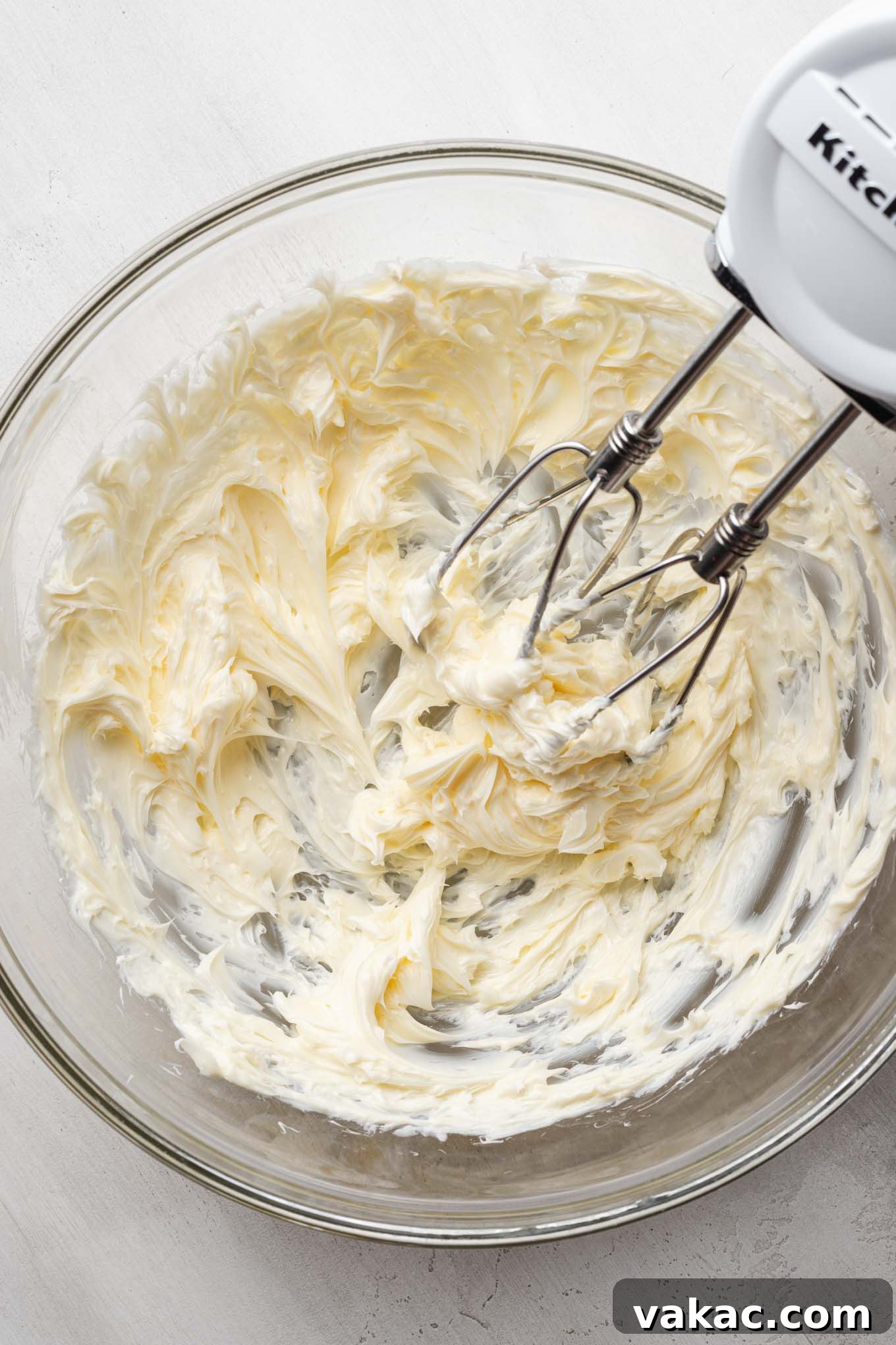 An overhead view of creamed butter in a glass mixing bowl with a hand mixer.