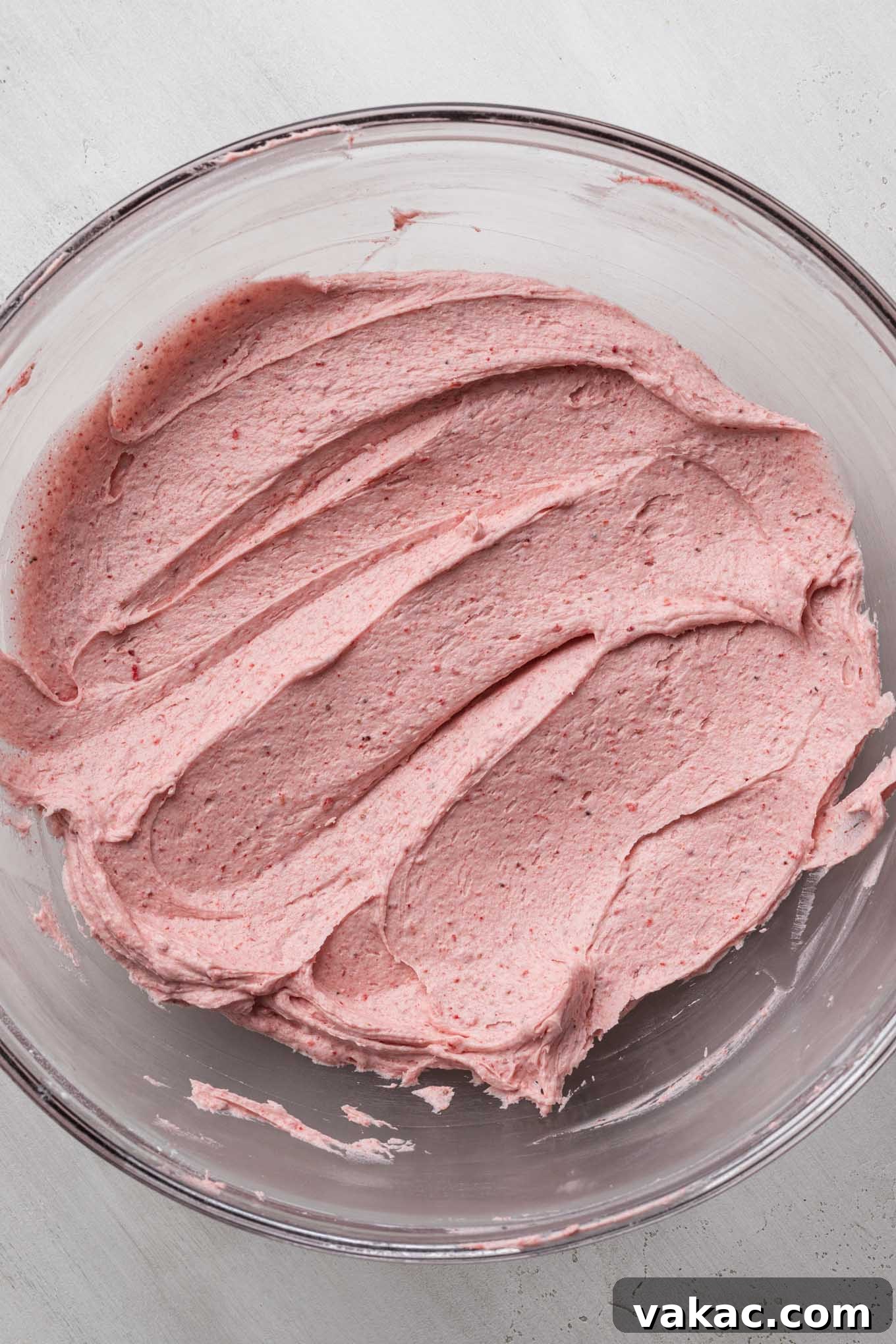 Strawberry frosting mixed together in a glass mixing bowl.