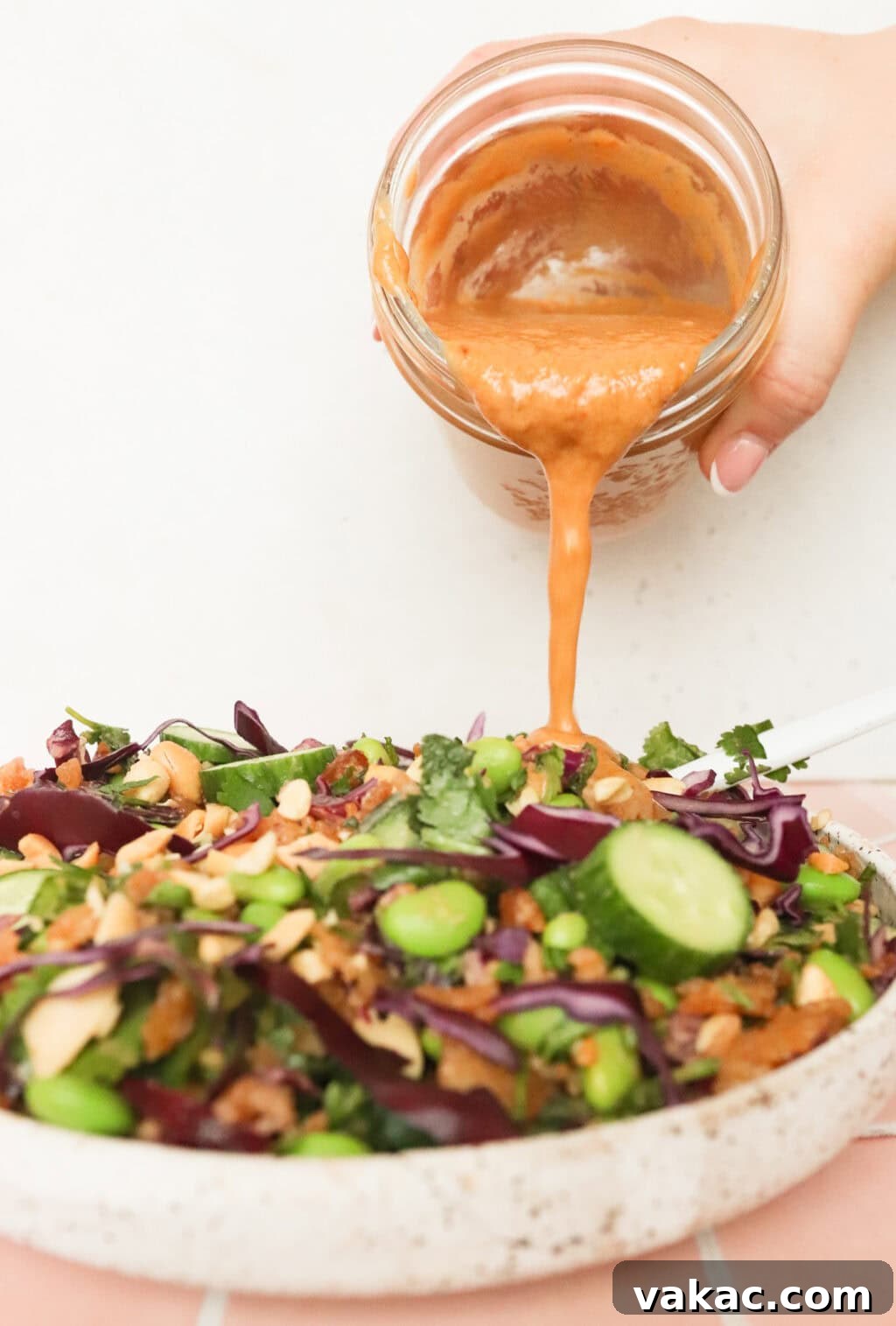 The creamy peanut lime salad dressing being poured from a glass mason jar onto the vibrant Thai Crispy Rice Salad in a bowl.