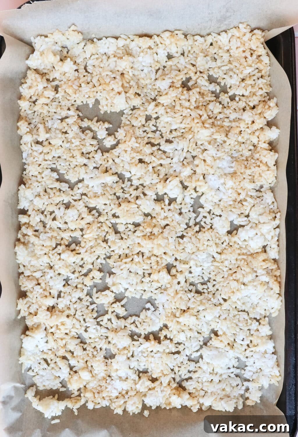 Overhead shot of the seasoned rice spread out on a baking sheet before being placed in the oven.