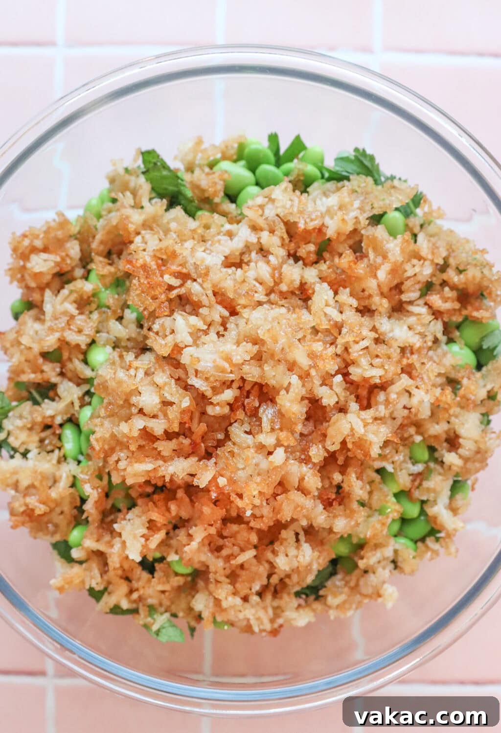 Overhead shot of the crispy rice crumbled on top of a bed of edamame, cucumber, and cabbage in a glass bowl, ready for dressing.