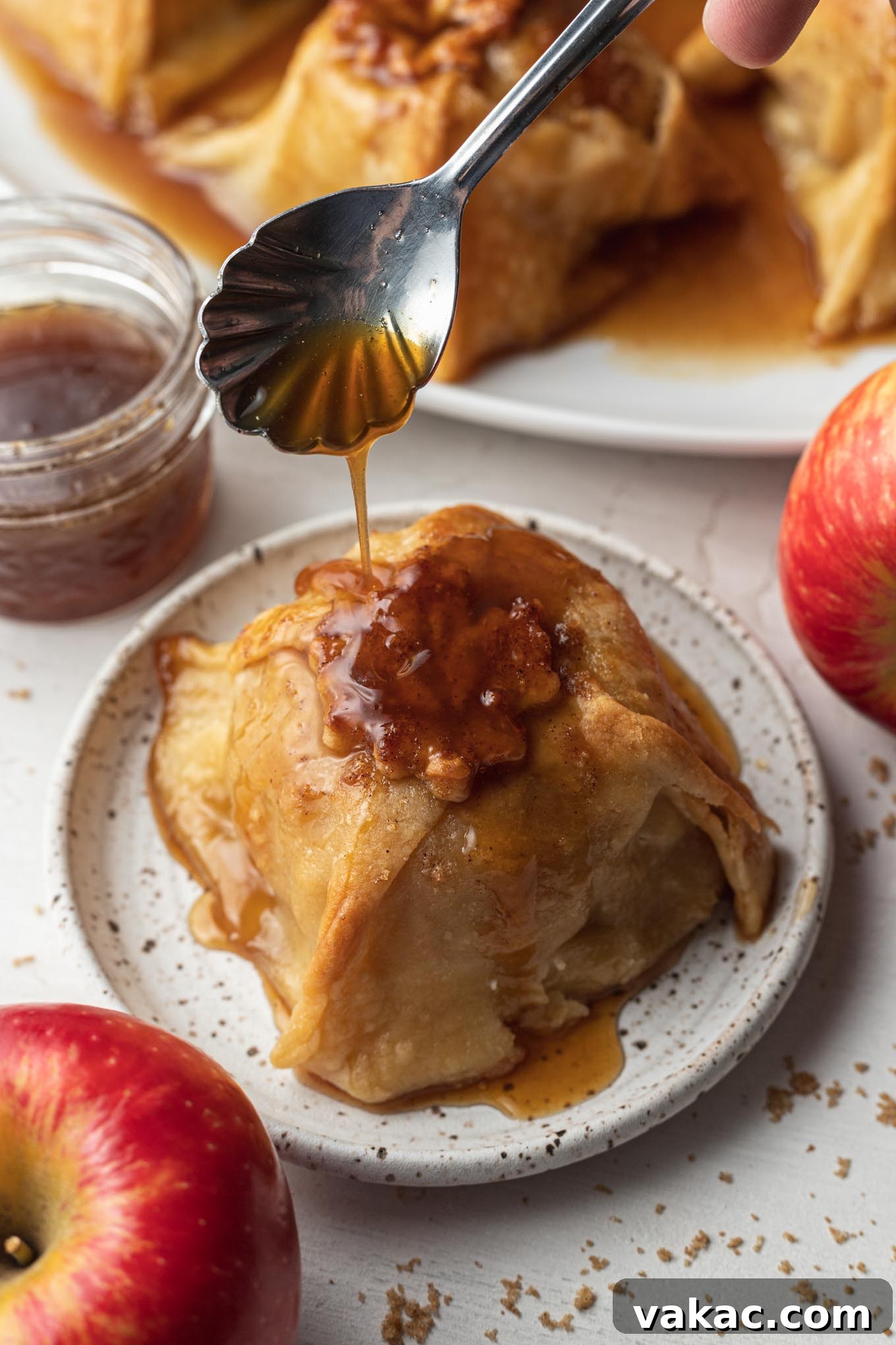 Golden Apple Delights 4 Sauce being spooned over a baked apple dumpling on a dessert plate.