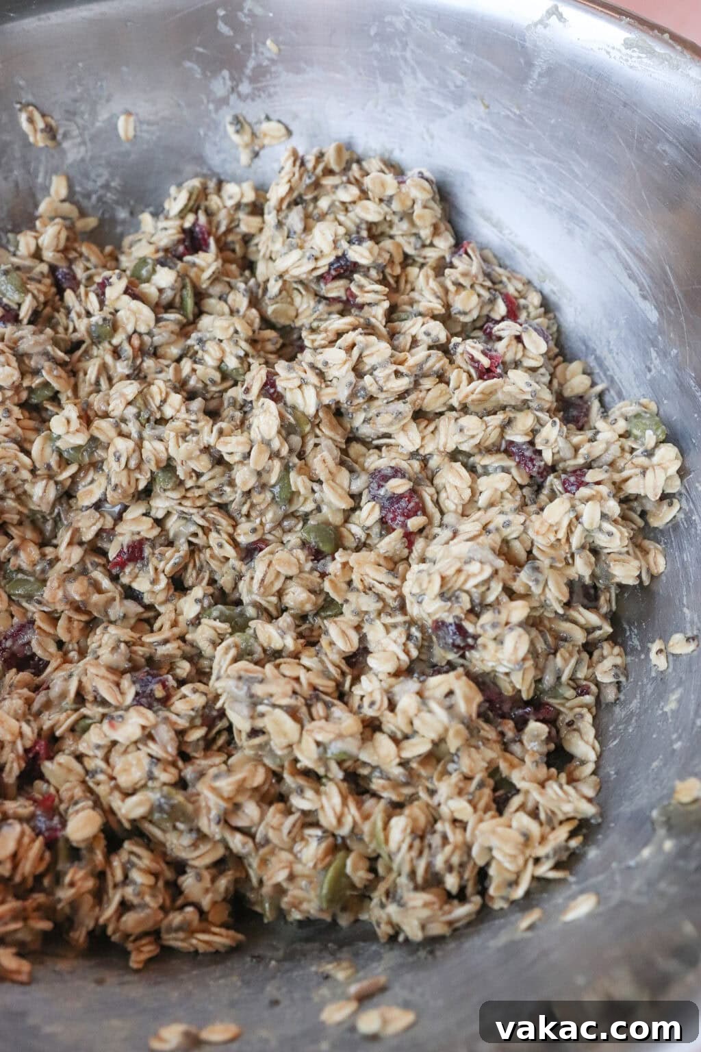 Allergy-Friendly Homemade Granola Bars 4 A large metal bowl filled with a mixture of oats, seeds, and dried cranberries. The ingredients appear to be mixed with a binding agent, creating a sticky and textured consistency.