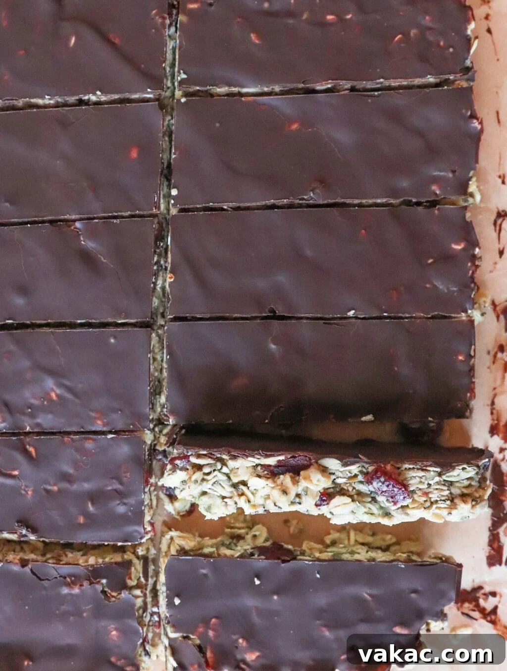 Allergy-Friendly Homemade Granola Bars 6 Close-up of chocolate-covered granola bars with visible nuts and oats on a cutting board. The bars are cut into rectangles, showing a rich, dark chocolate topping. One piece appears slightly pulled away from the rest.