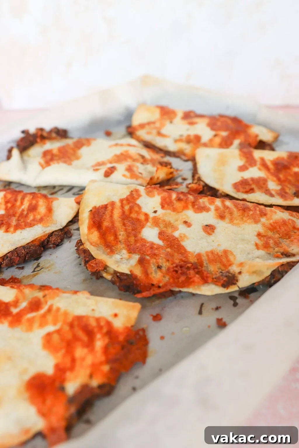 Close-up of fried tacos on a baking sheet lined with parchment paper. The tacos are golden with some browned spots, suggesting they were baked or fried to a crisp. The background is out of focus, emphasizing the tacos.