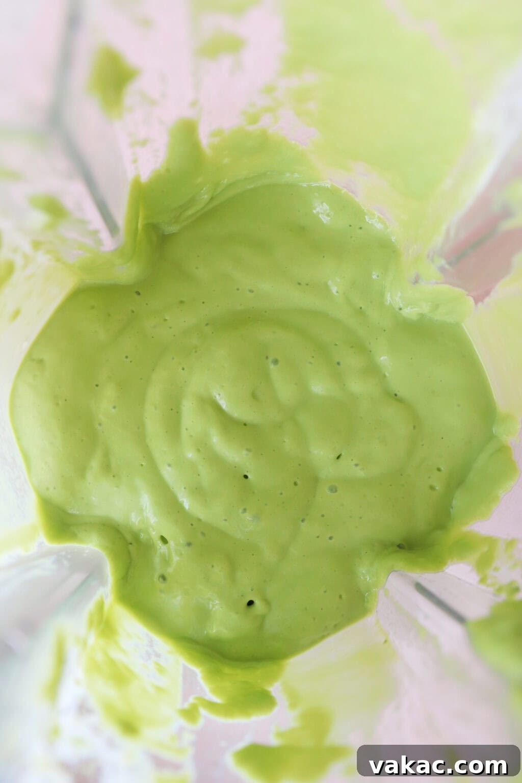 A close-up view of the interior of a blender, filled with a smooth, creamy, and pale green mixture. Swirls of the blended ingredients cling to the sides of the container, indicating a perfectly emulsified and thick consistency, ready to be poured and enjoyed.