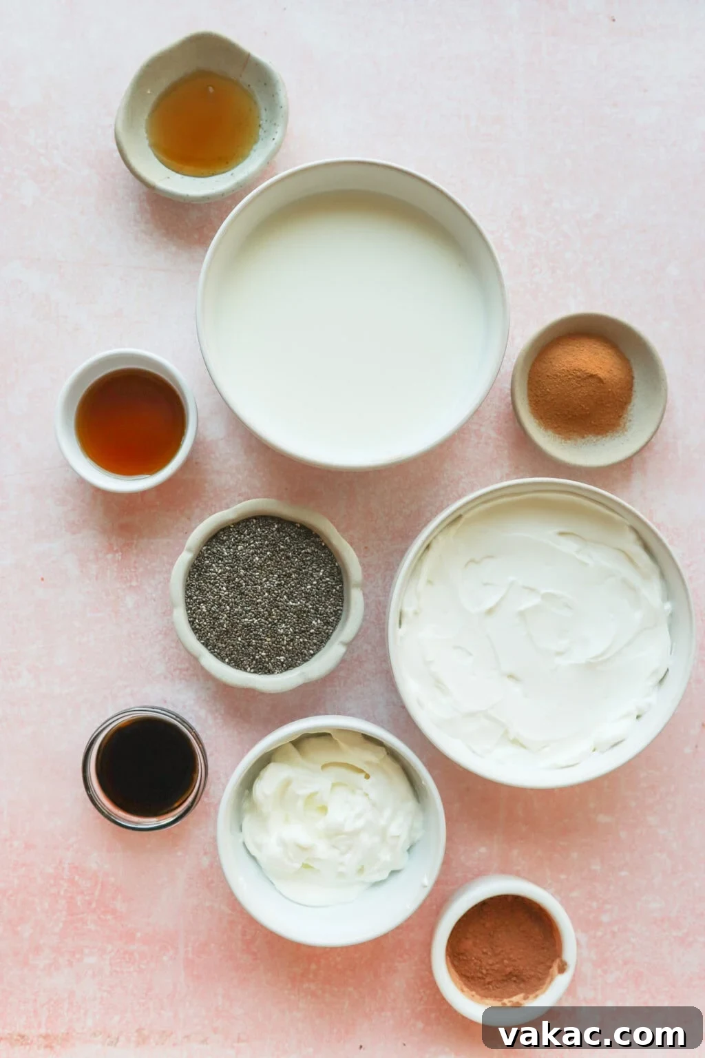 Dreamy Protein Tiramisu Chia Pudding with Yogurt 3 A flat lay of various ingredients in small bowls on a pink surface, including milk, yogurt, chia seeds, cocoa powder, greek yogurt, vanilla extract, and honey or syrup.