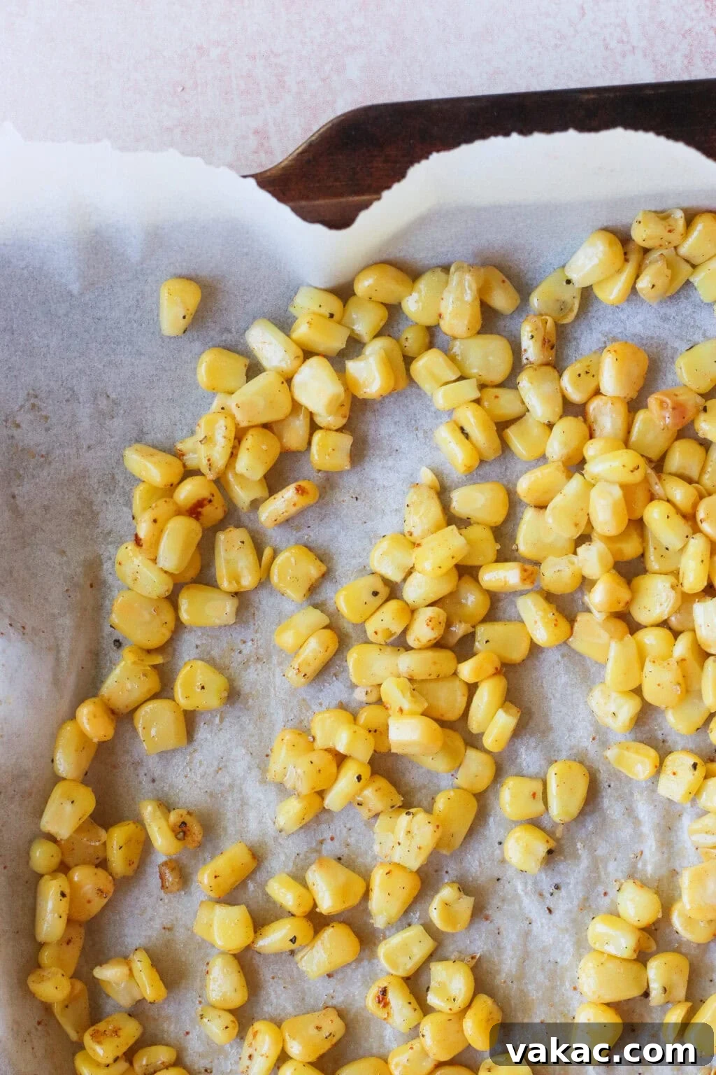 Golden roasted corn kernels scattered on a parchment-lined baking tray, lightly browned and seasoned, with some empty space and a corner of the tray visible.
