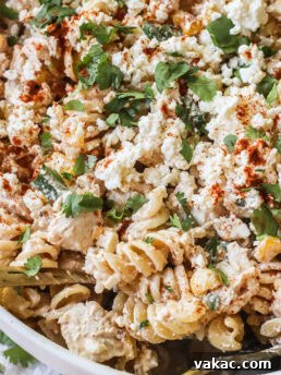A close-up of a creamy Elote-inspired pasta salad with rotini, shredded chicken, crumbled cotija cheese, fresh cilantro, and a sprinkle of paprika, served in a white bowl.