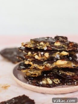 A top-down shot of a single piece of homemade Snickers date bark with visible layers of chocolate, peanuts, and date, garnished with flaky sea salt.