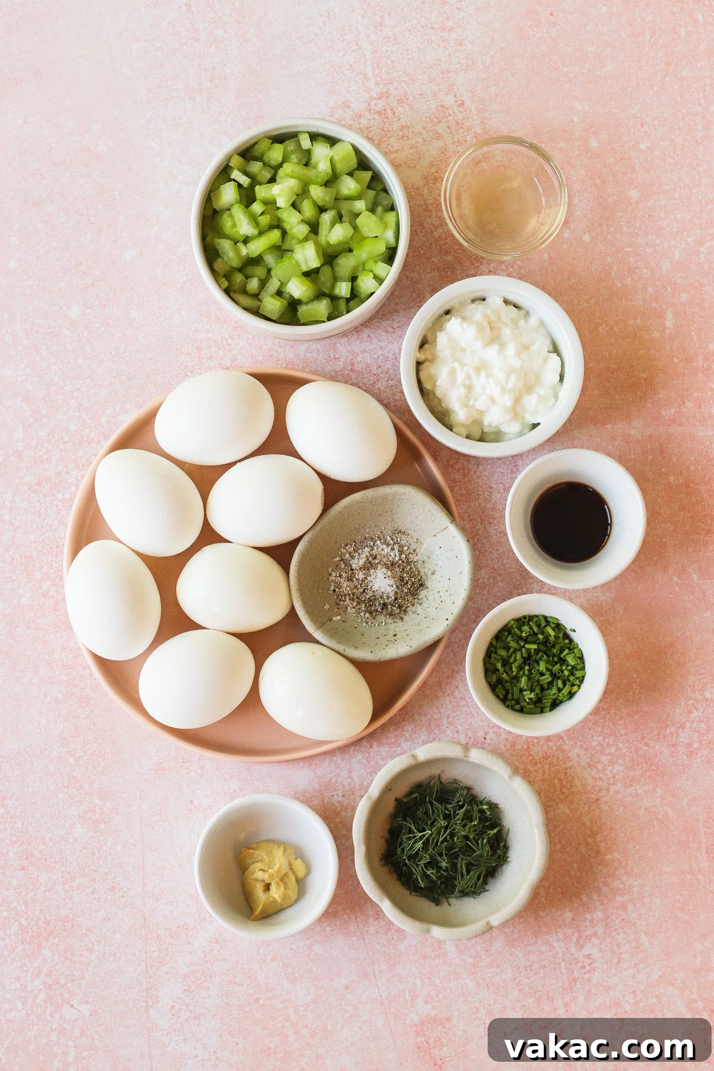 Creamy High Protein Cottage Cheese Egg Salad No Mayo 3 A flat lay of ingredients on a pink surface: hard-boiled eggs, chopped celery, cottage cheese, chives, dill, vinegar, mustard, Worcestershire sauce, and a small dish of salt and pepper.
