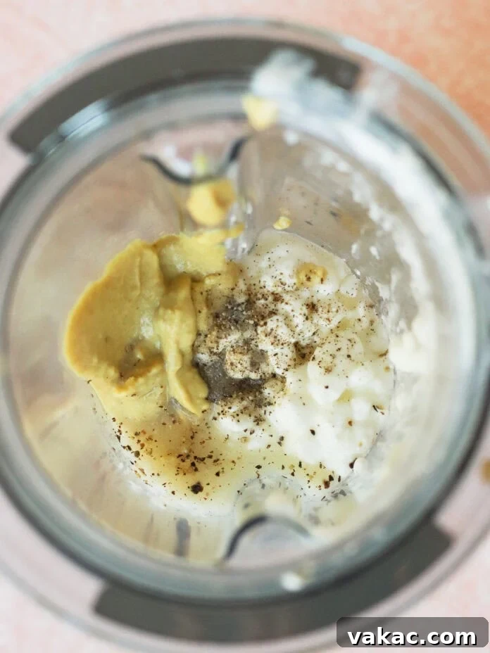 Creamy High Protein Cottage Cheese Egg Salad No Mayo 5 A blender with cottage cheese, mustard, black pepper, and seasonings inside, viewed from above on a pink countertop.
