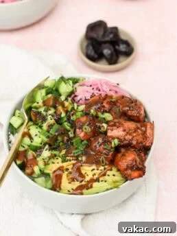A bowl with sliced avocado, cucumber, marinated tofu, pickled onions, chopped scallions, black sesame seeds, and sauce, served on a light cloth with a small bowl of prunes in the background.