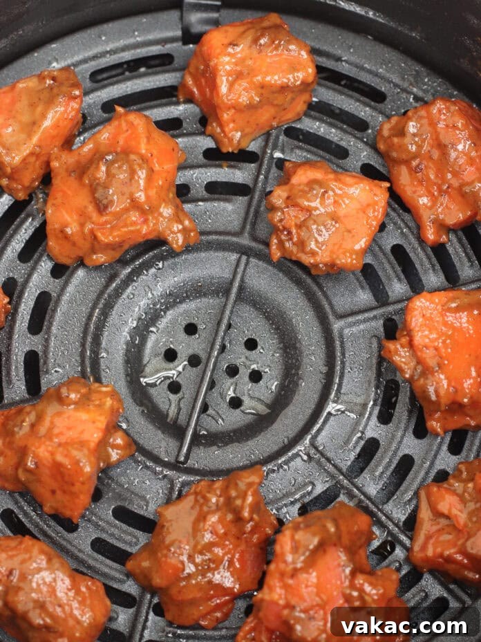 Quick Air Fryer Salmon Bowls: Sweet and Spicy Prune Delight 8 Perfectly marinated chunks of salmon arranged in a single, even layer inside an air fryer basket, ready to be cooked to perfection. The spacing ensures optimal air circulation for even crisping.