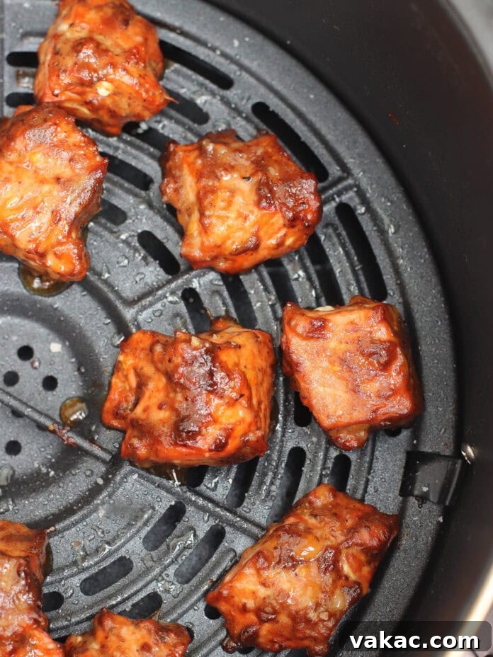 Quick Air Fryer Salmon Bowls: Sweet and Spicy Prune Delight 9 Crispy, perfectly cooked barbecue-glazed pieces of salmon are arranged invitingly in an air fryer basket, showing a rich, caramelized exterior with some beautiful grill marks and bubbling glaze.