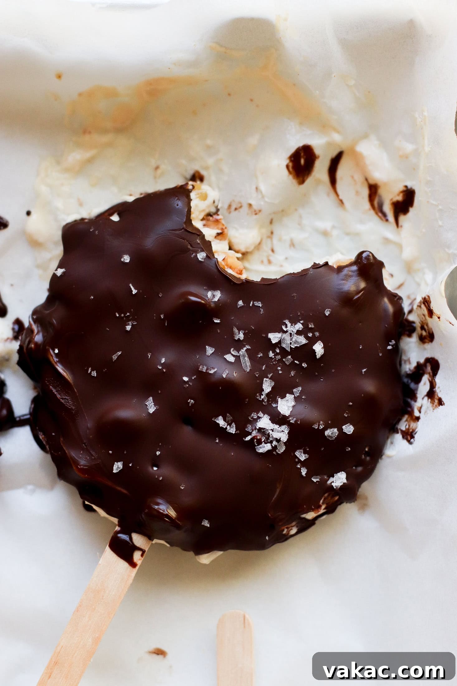 Creamy Chocolate Peanut Butter Fro Yo Treats 2 A chocolate-covered ice cream bar with a bite taken out, sprinkled with flaky sea salt, rests on parchment paper with some melted chocolate and ice cream visible around it.