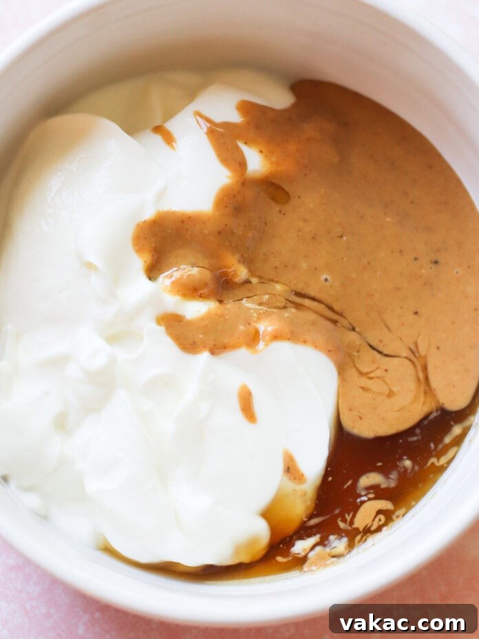 Creamy Chocolate Peanut Butter Fro Yo Treats 4 A white bowl filled with thick white yogurt, creamy brown peanut butter, and golden syrup, each ingredient slightly blending together but still distinct.