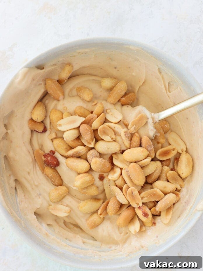 Creamy Chocolate Peanut Butter Fro Yo Treats 5 A bowl of creamy peanut butter mixture with roasted peanuts on top, being stirred with a spoon.