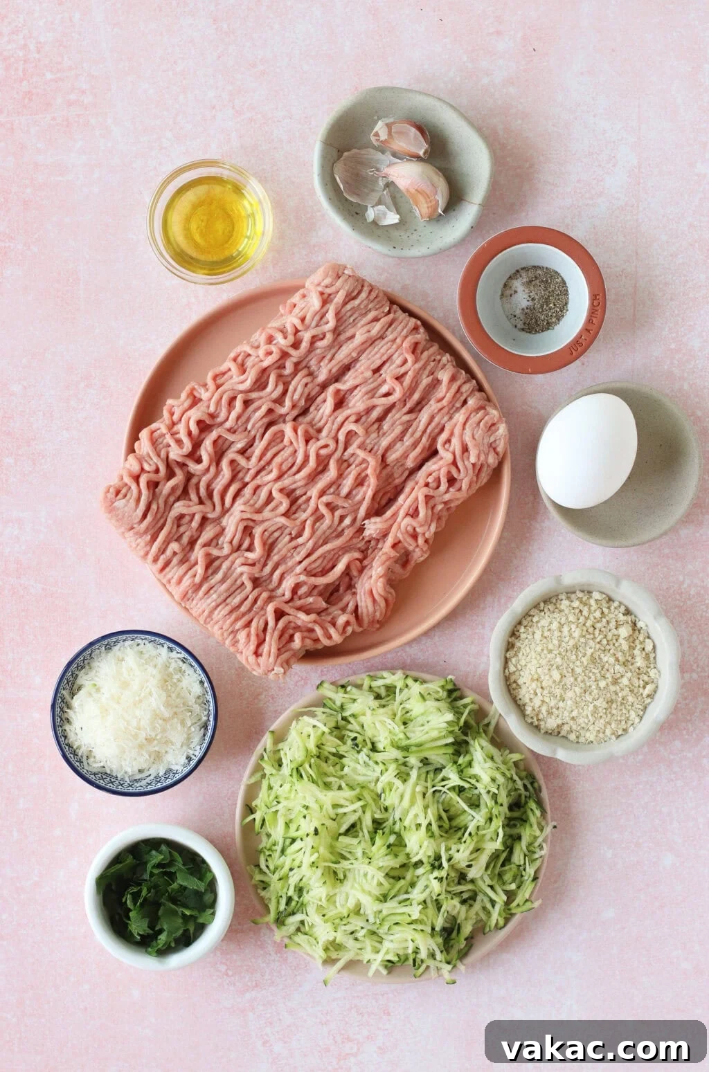 Quick Sheet Pan Turkey Zucchini Meatballs Tender and Juicy 3 A flat lay photograph displays a vibrant collection of fresh ingredients for turkey zucchini meatballs, meticulously arranged in small bowls on a light pink surface. Ingredients include raw ground turkey, finely shredded zucchini, grated Parmesan cheese, a fresh egg, light panko breadcrumbs, fragrant chopped herbs, olive oil, garlic cloves, and various seasonings. This image highlights the wholesome components and ease of preparation.