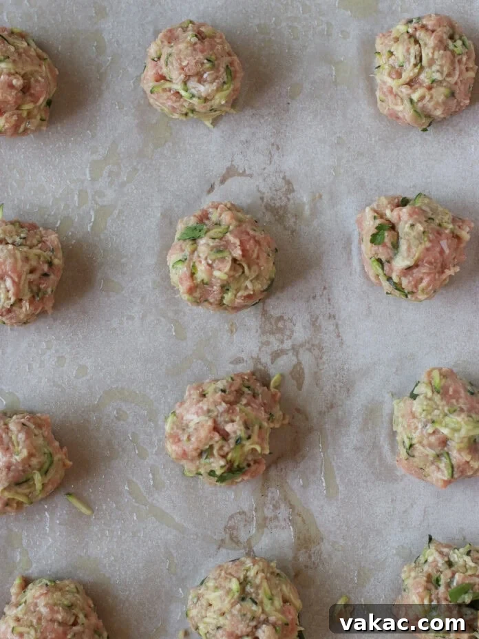 Quick Sheet Pan Turkey Zucchini Meatballs Tender and Juicy 5 Raw, unbaked turkey and zucchini meatballs, uniformly shaped and mixed with herbs and shredded vegetables, are neatly arranged in rows on a parchment-lined baking sheet, prepared and ready to be cooked.