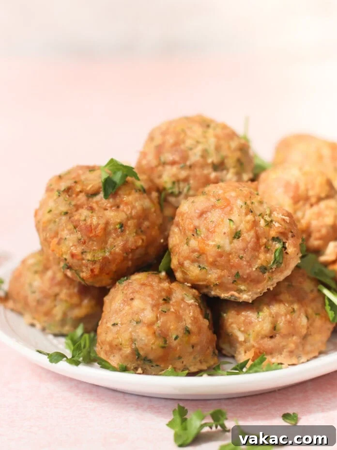 Quick Sheet Pan Turkey Zucchini Meatballs Tender and Juicy 6 A plate stacked high with beautifully golden-brown baked turkey and zucchini meatballs, lightly garnished with fresh chopped parsley, sits invitingly on a light pink surface with more parsley scattered around, ready to be served.