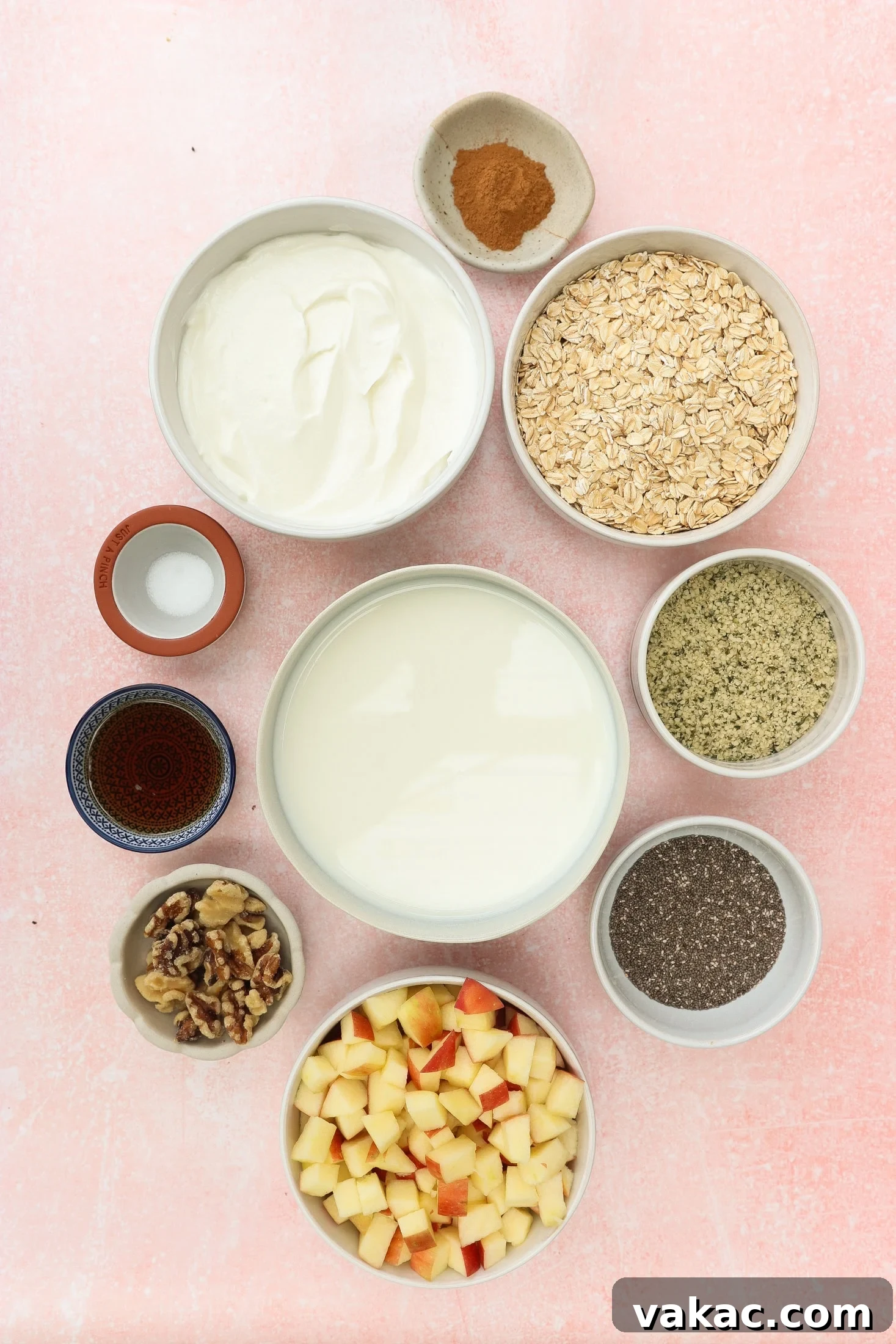 Protein-Packed Apple Cinnamon Overnight Oats 3 Bowls containing yogurt, rolled oats, milk, diced apples, walnuts, chia seeds, hemp seeds, maple syrup, cinnamon, and a pinch of salt, arranged neatly on a light pink background.