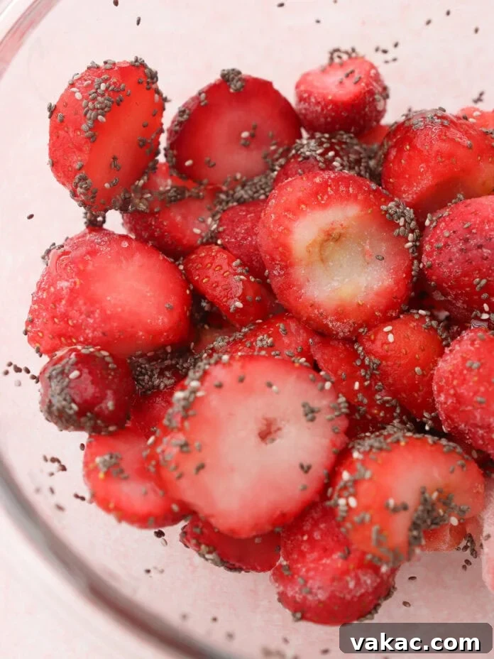 Instant Strawberry Greek Yogurt Stack 5 A clear glass bowl showcasing sliced strawberries generously coated in tiny chia seeds, awaiting preparation.