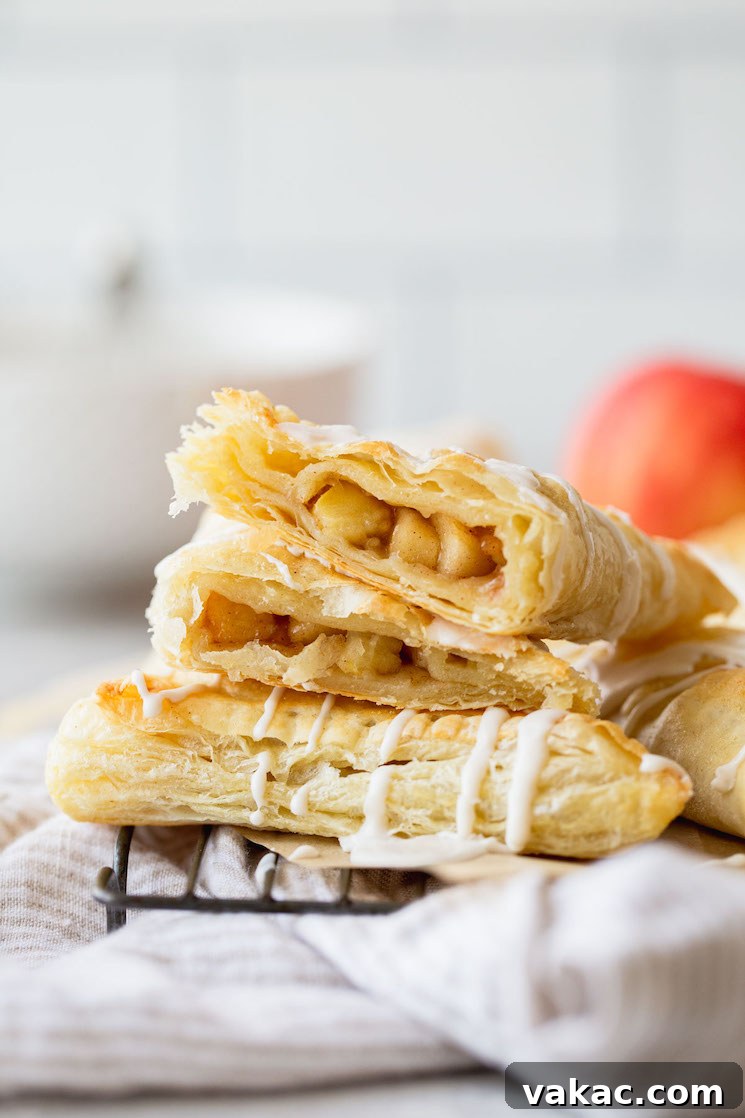 A stack of golden brown apple turnovers with one cut in half, revealing the luscious apple filling.