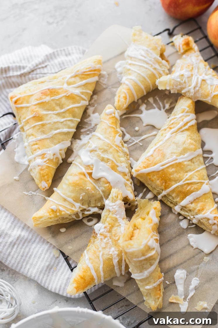 A batch of freshly baked apple turnovers arranged on a cooling rack and generously topped with a maple cinnamon glaze.