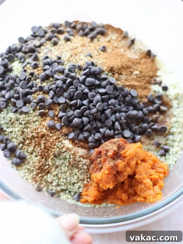 Speedy Pumpkin Spice Almond Flour Protein Bites 4 A clear bowl filled with chocolate chips, pumpkin puree, hemp seeds, ground spices, and flour, ready to be mixed for baking.