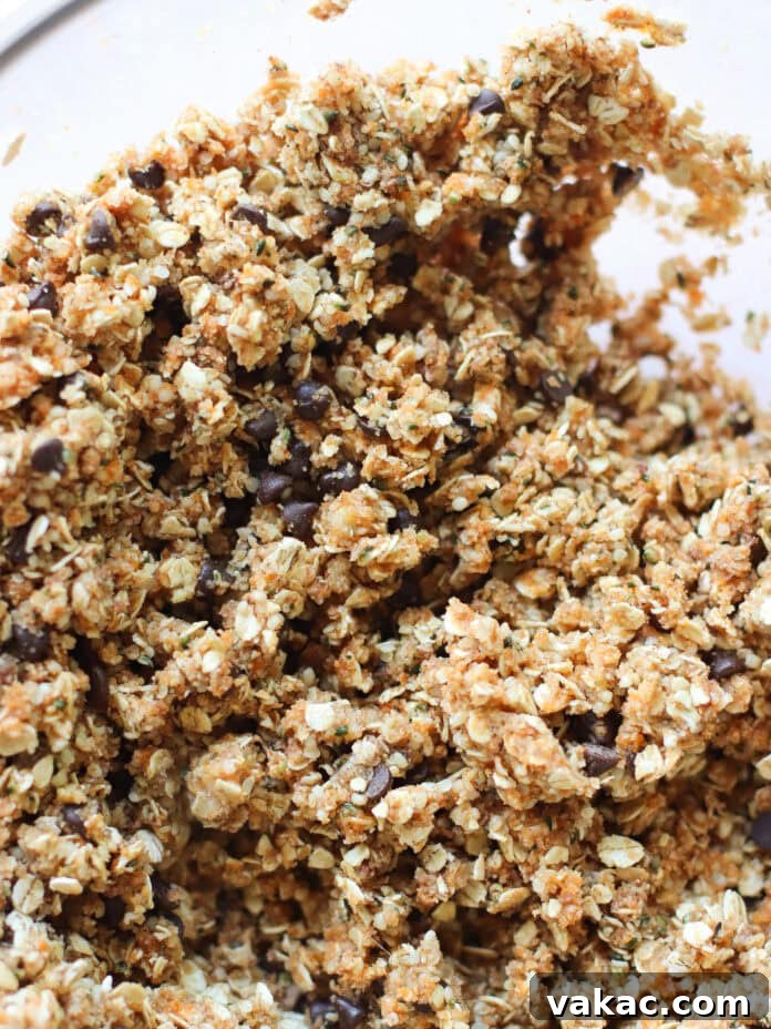 Speedy Pumpkin Spice Almond Flour Protein Bites 5 A close-up of a bowl filled with a crumbly mixture of oats, chocolate chips, and other baking ingredients, likely cookie or granola bar dough.