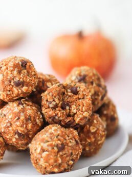 A stack of oat and chocolate chip energy bites sits on a white plate, with a blurred orange pumpkin in the background.