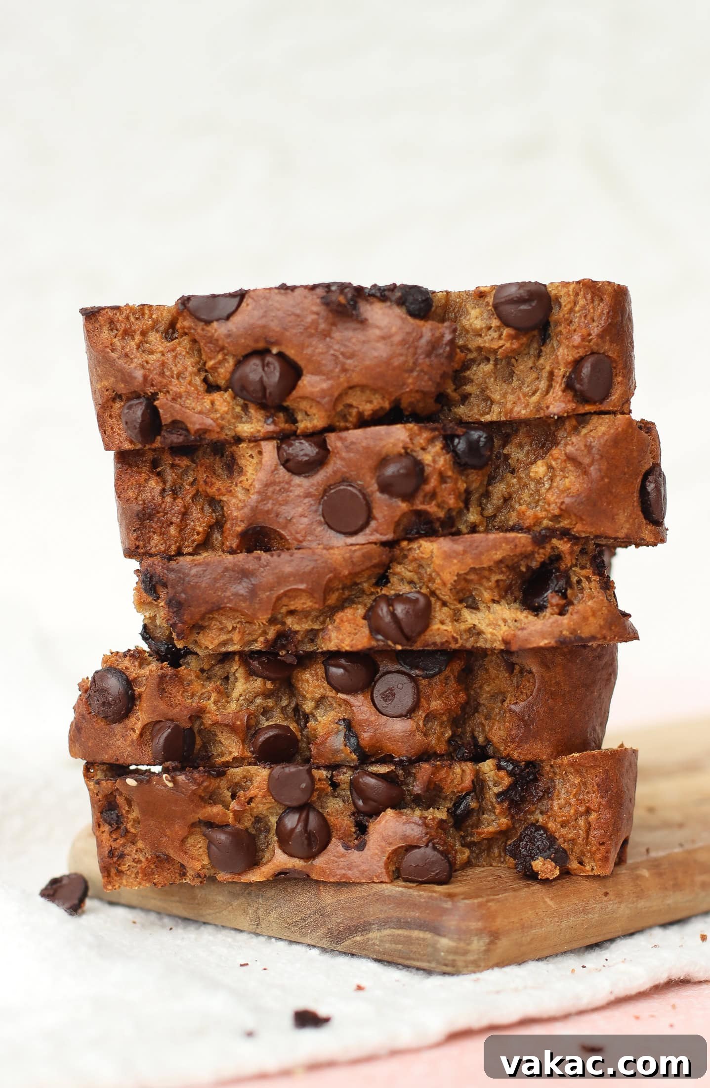 Super Moist Cottage Cheese Banana Bread Protein Boost 4 A stack of five thick, irresistible slices of chocolate chip cottage cheese banana bread artfully arranged on a wooden board. Each slice is studded with abundant, melted chocolate chips, highlighting the bread's moist and tender interior. The background is softly blurred, emphasizing the deliciousness of the foreground.