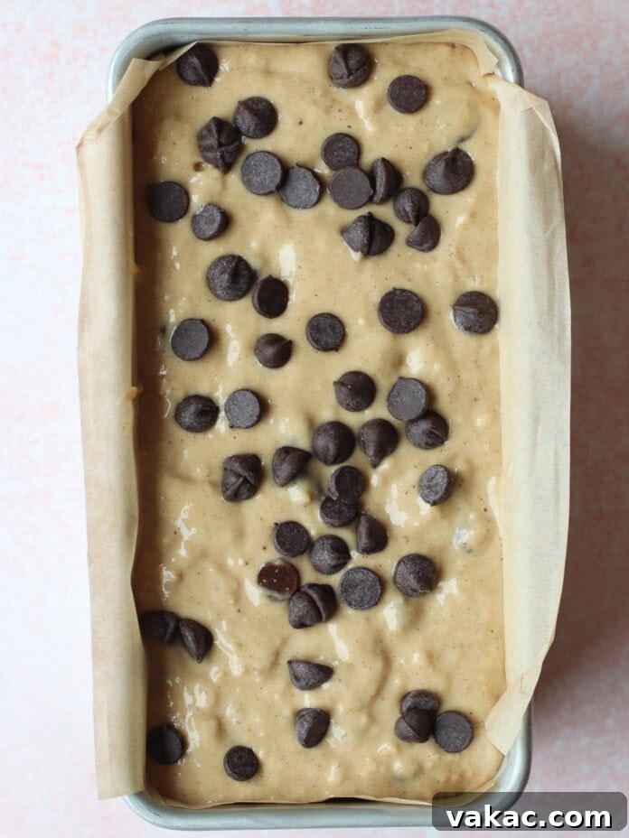 Super Moist Cottage Cheese Banana Bread Protein Boost 7 A loaf pan, neatly lined with parchment paper, is filled with the unbaked banana bread batter, generously topped with scattered chocolate chips, eagerly awaiting its journey to the oven.