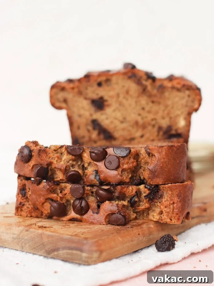 Super Moist Cottage Cheese Banana Bread Protein Boost 8 Two enticing slices of golden-brown chocolate chip banana bread rest on a wooden board, with the remainder of the freshly baked loaf in the background. The bread glistens with melted chocolate chips, promising a delicious experience.