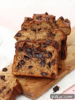 Sliced chocolate chip banana bread on a wooden board, showing moist texture and visible chocolate chips in each slice.