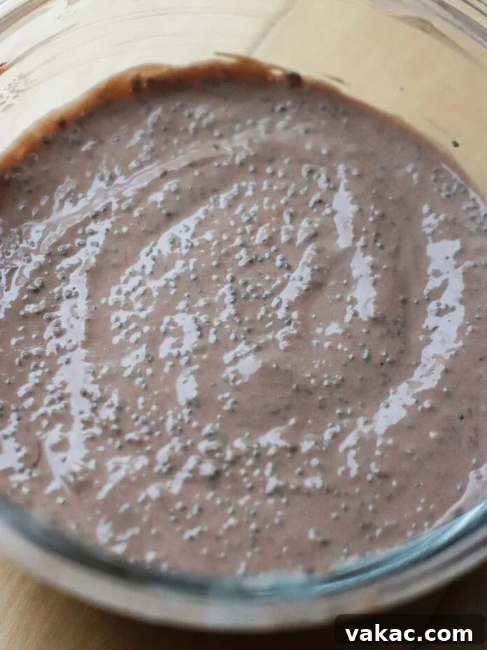 Velvet Chocolate Chia Protein Pudding with Greek Yogurt 5 A glass bowl filled with chocolate chia pudding mixture sits on a light wooden surface. The pudding is creamy with visible chia seeds evenly distributed throughout.