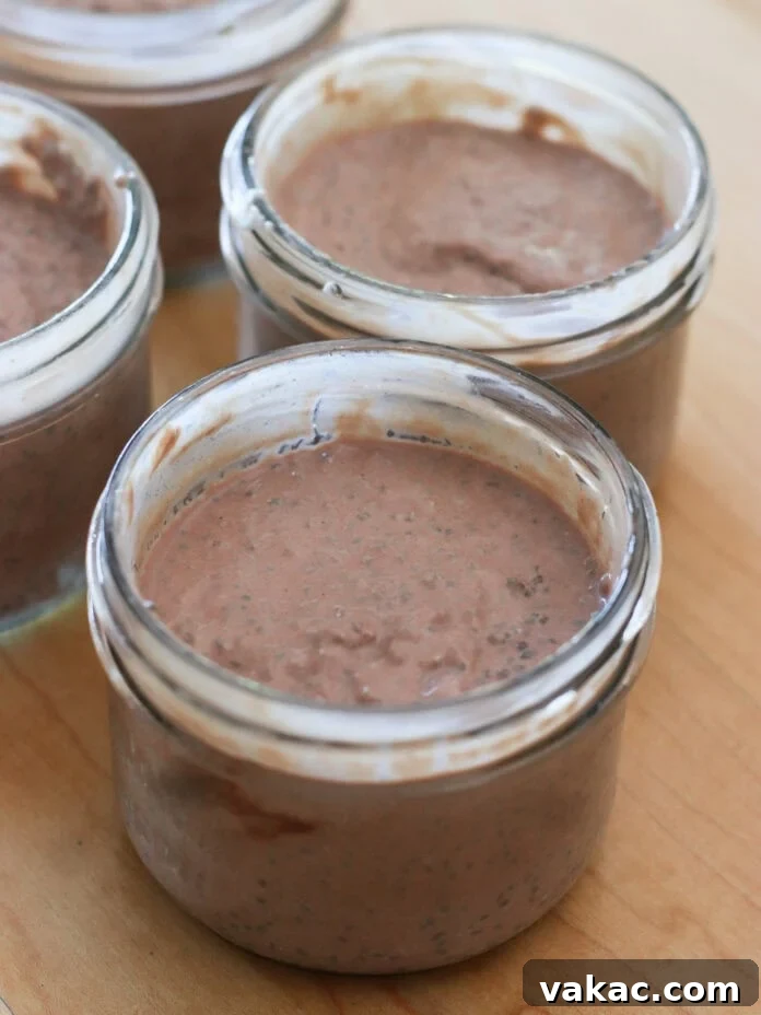 Velvet Chocolate Chia Protein Pudding with Greek Yogurt 6 Four small glass jars filled with chocolate chia pudding are placed on a wooden surface. The pudding is brown and has a creamy texture with visible chia seeds.