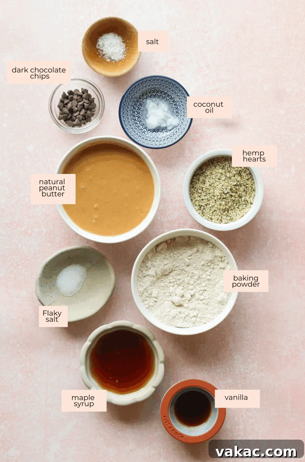 No-Bake Peanut Butter Oat Flour Energy Bites 3 A flat lay of labeled ingredients in bowls on a pink surface: salt, dark chocolate chips, coconut oil, natural peanut butter, hemp hearts, baking powder, flaky salt, maple syrup, and vanilla.