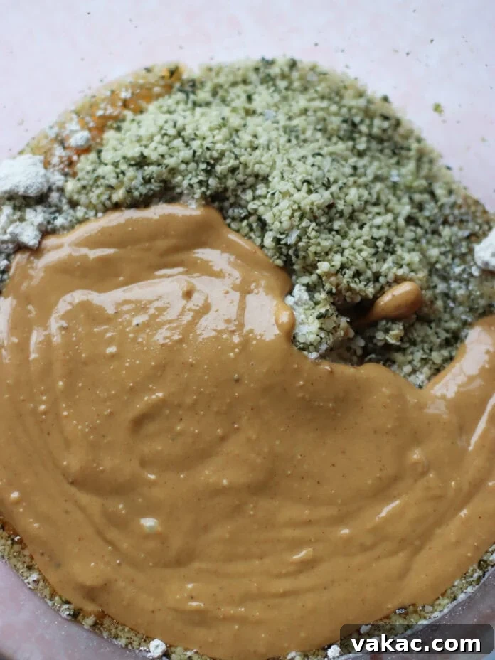 No-Bake Peanut Butter Oat Flour Energy Bites 4 A close-up of a glass mixing bowl containing a mound of hemp seeds, creamy peanut butter, and some dry ingredients, ready to be mixed together.