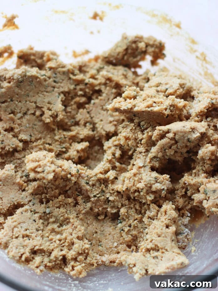 No-Bake Peanut Butter Oat Flour Energy Bites 5 A close-up of cookie dough in a glass mixing bowl, showing a coarse and crumbly texture with visible flecks of ingredients throughout.