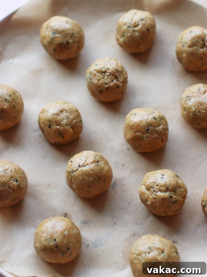 No-Bake Peanut Butter Oat Flour Energy Bites 6 Sixteen round dough balls evenly spaced on a baking sheet lined with parchment paper, ready to be baked. The dough appears to have herbs or seasoning mixed in.